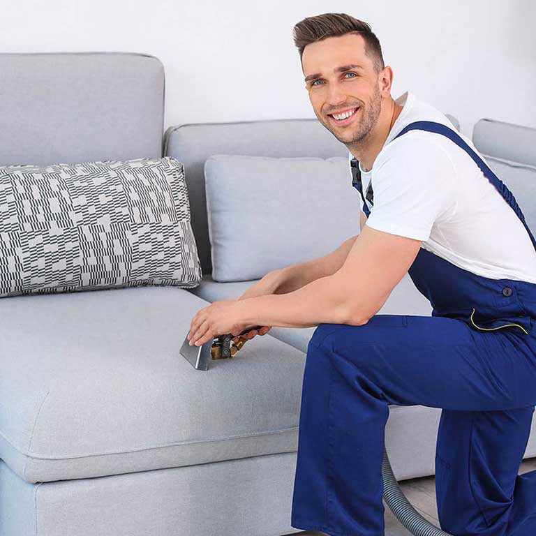 Carpet worker kneeling in front of a couch as he cleans it