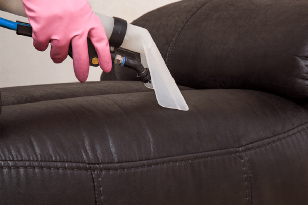 Person with a pink glove vacuuming a leather couch